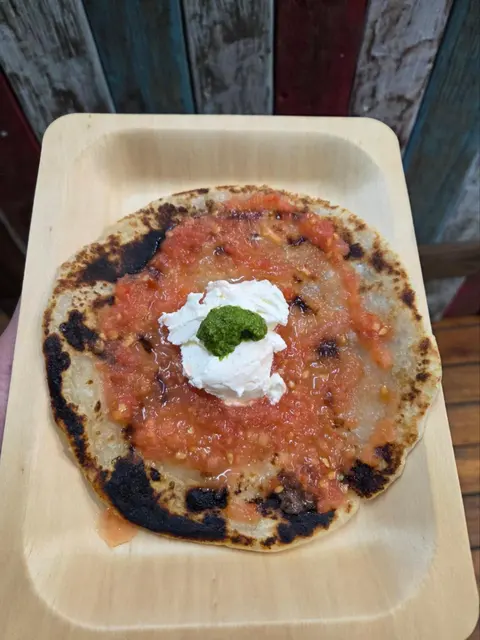 Malawach flatbread with grated tomato, labneh and green zhoug on a timber tray, colourful painted-plank wall behind