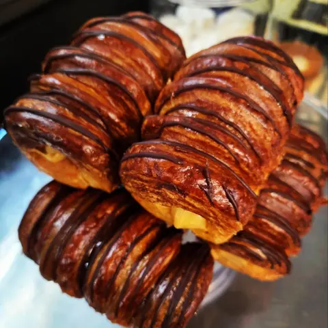 Stack of glossy banoffee croissants with chocolate drizzle stripes and caramel filling, close up