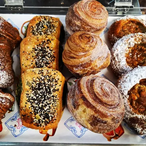 Overhead of the pastry cabinet tray: seeded savoury pastries, spiral cruffin-style croissants and sugar-dusted filled pastries on printed paper