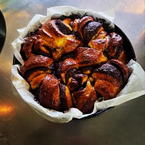 Round chocolate babka, glossy twisted crown in a paper-lined tin on the steel bench