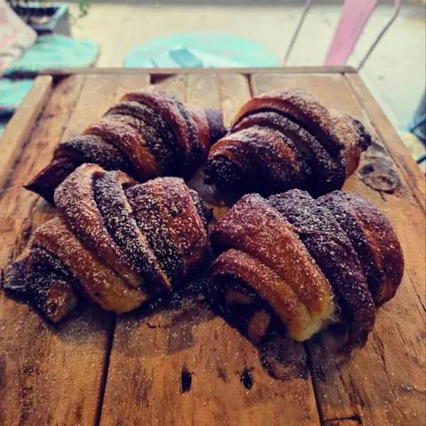 Chocolate rugelach (rogelach) dusted with icing sugar on a rustic timber crate, turquoise table and pink chair behind