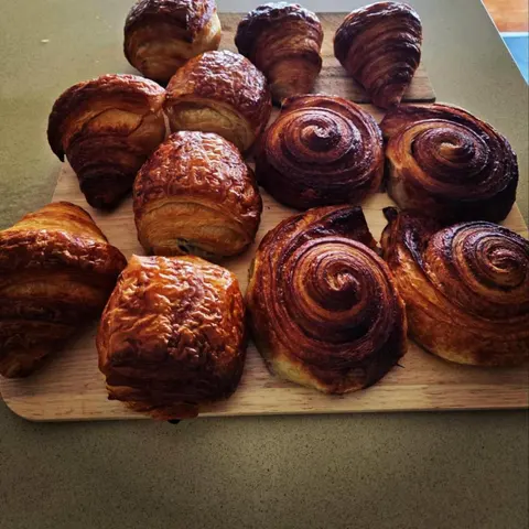 Board of house-baked laminated pastries: croissants, pain au chocolat and glossy spiral pastries, on a stone bench