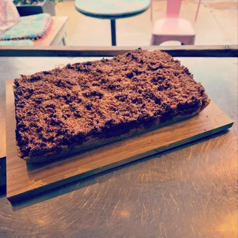 Coconut and raspberry slice on a timber board on the steel bench, pink chair and cafe table on the verandah behind