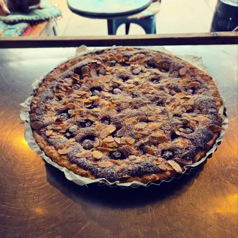 Almond and blueberry tart in a fluted tin on a steel bench; a dachshund lies on the turquoise cushions behind
