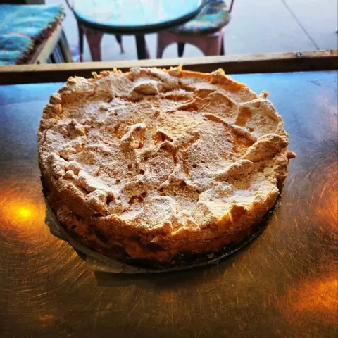 Tall apricot meringue pie dusted with icing sugar on a steel bench, verandah cafe chairs behind
