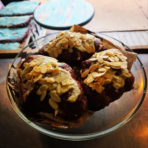 Glass bowl of chocolate almond croissants on newsprint paper, turquoise cafe table and cushions behind