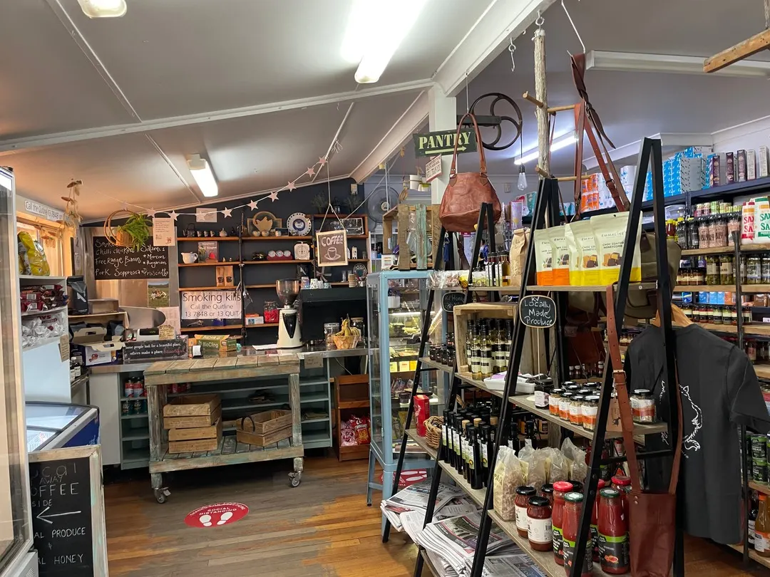 Inside the store: timber floors, a pantry sign, shelves of sauces and preserves, bread and deli counter at the back.