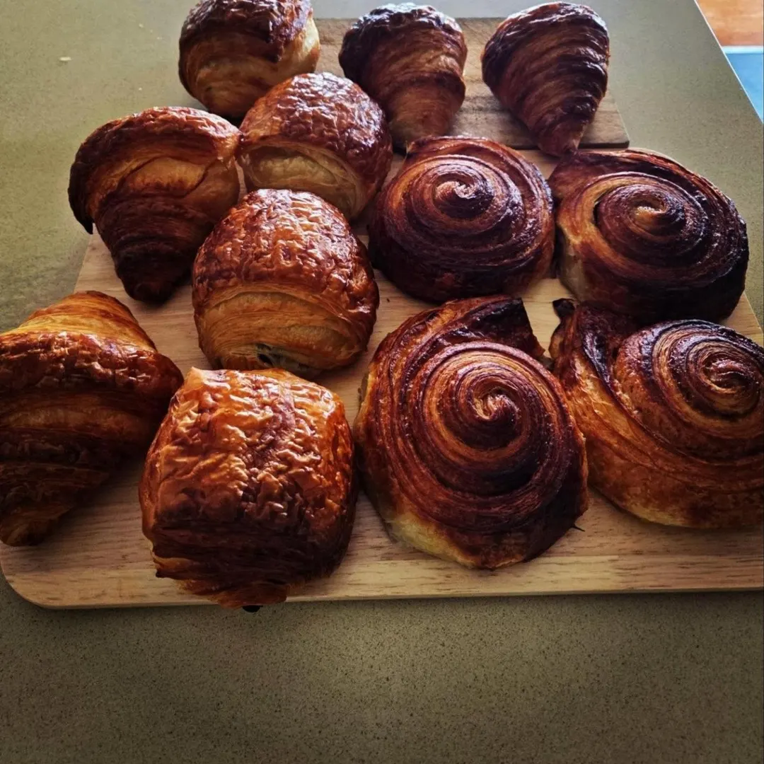 A board of house-baked laminated pastries: croissants, pain au chocolat and glossy spirals.