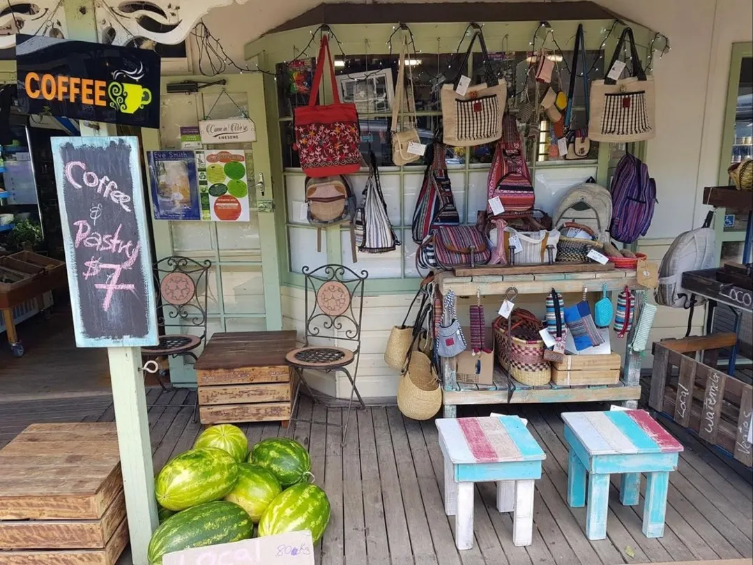 The front verandah: a COFFEE sign, a chalkboard, wrought-iron chairs, woven bags hanging in the window, pastel striped stools and a pile of watermelons.